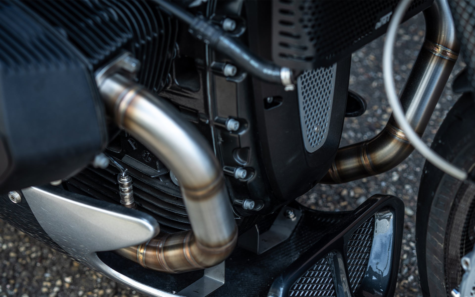 Front close-up of the MAD Exhausts BMW R nineT header pipes routed past the engine, showing heat-blued stainless steel finish