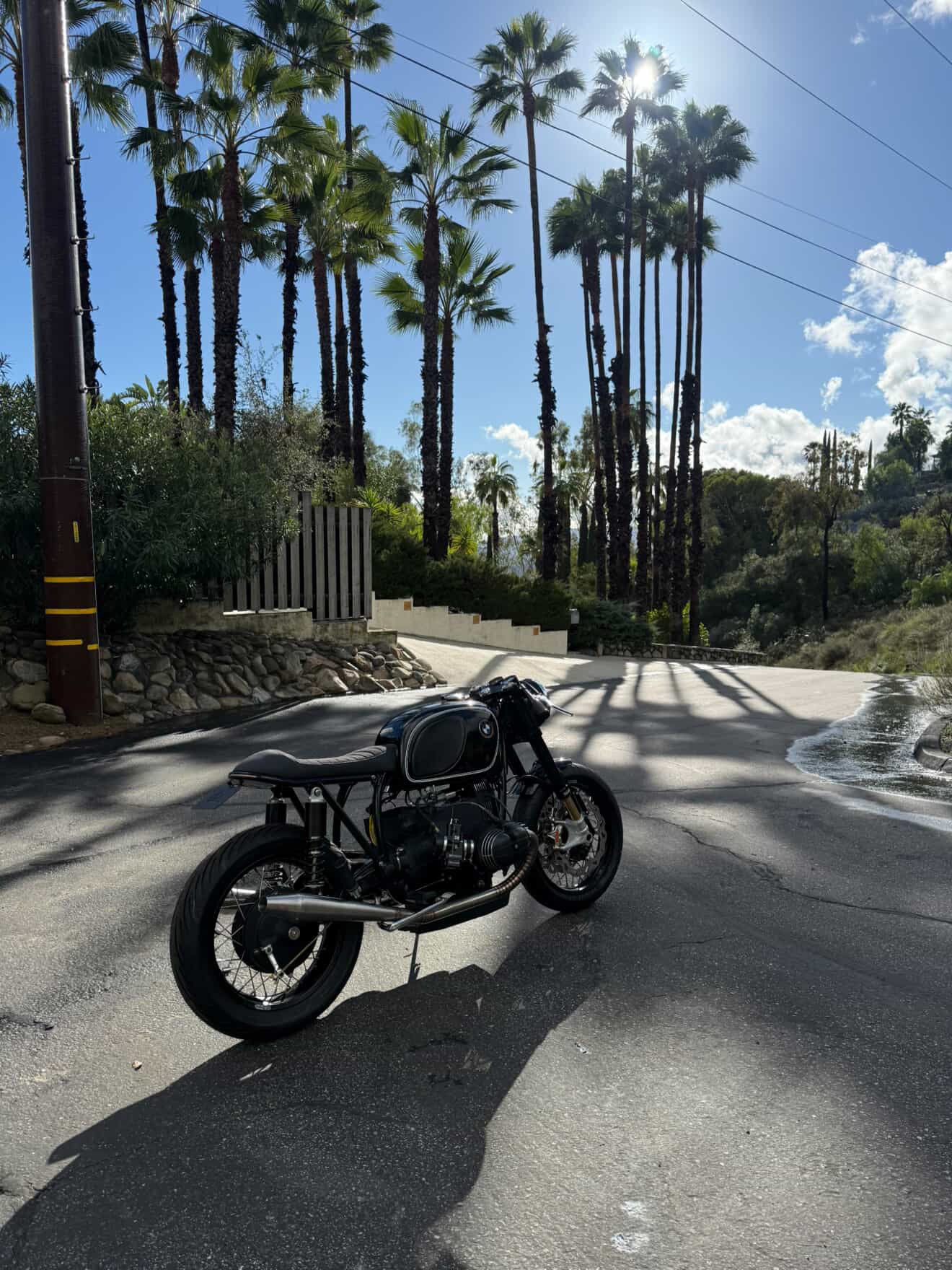 BMW airhead cafe racer with MAD Exhausts system parked on a palm-lined road, lifestyle photo
