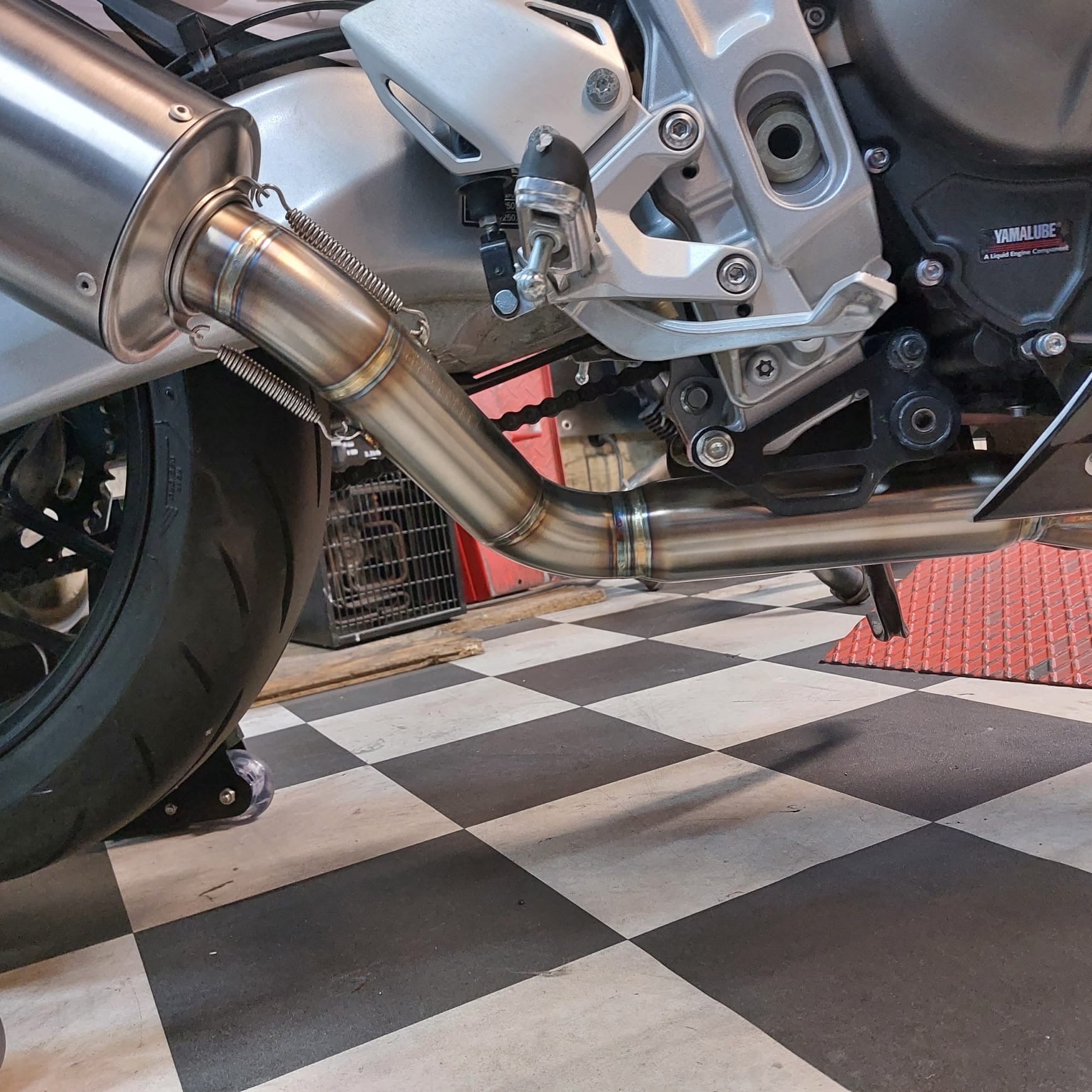 Low-angle view of the MAD-Ex silencer and spring-mounted mid-pipe on the Yamaha XSR900 GP, next to the rear wheel