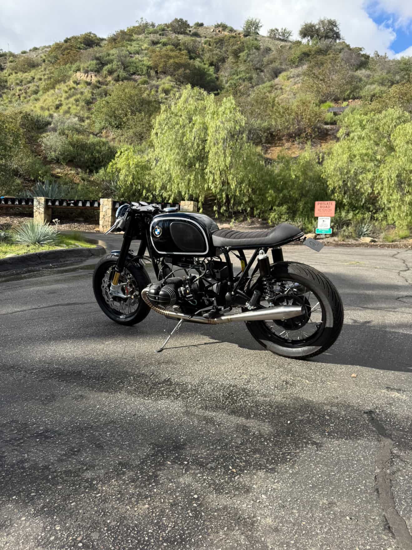 Full left-side view of the BMW airhead cafe racer with the MAD Exhausts system running along the frame, hillside road