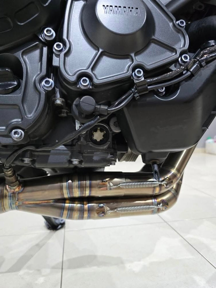 MAD Exhausts stainless steel headers joining under the Yamaha CP3 three-cylinder engine, spring-mounted connections visible