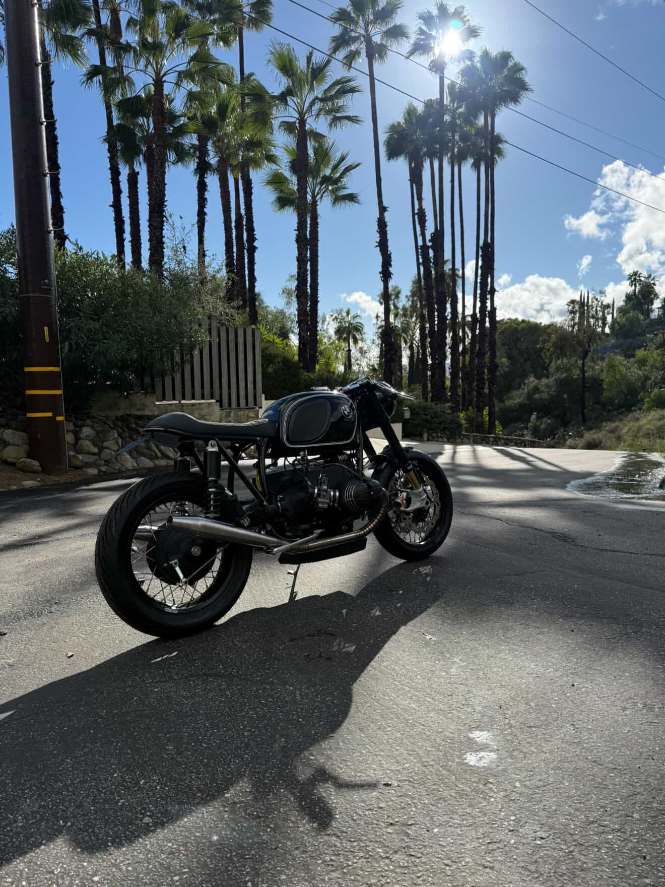 BMW airhead cafe racer with MAD Exhausts system, backlit rear three-quarter view on a sunny palm-lined road