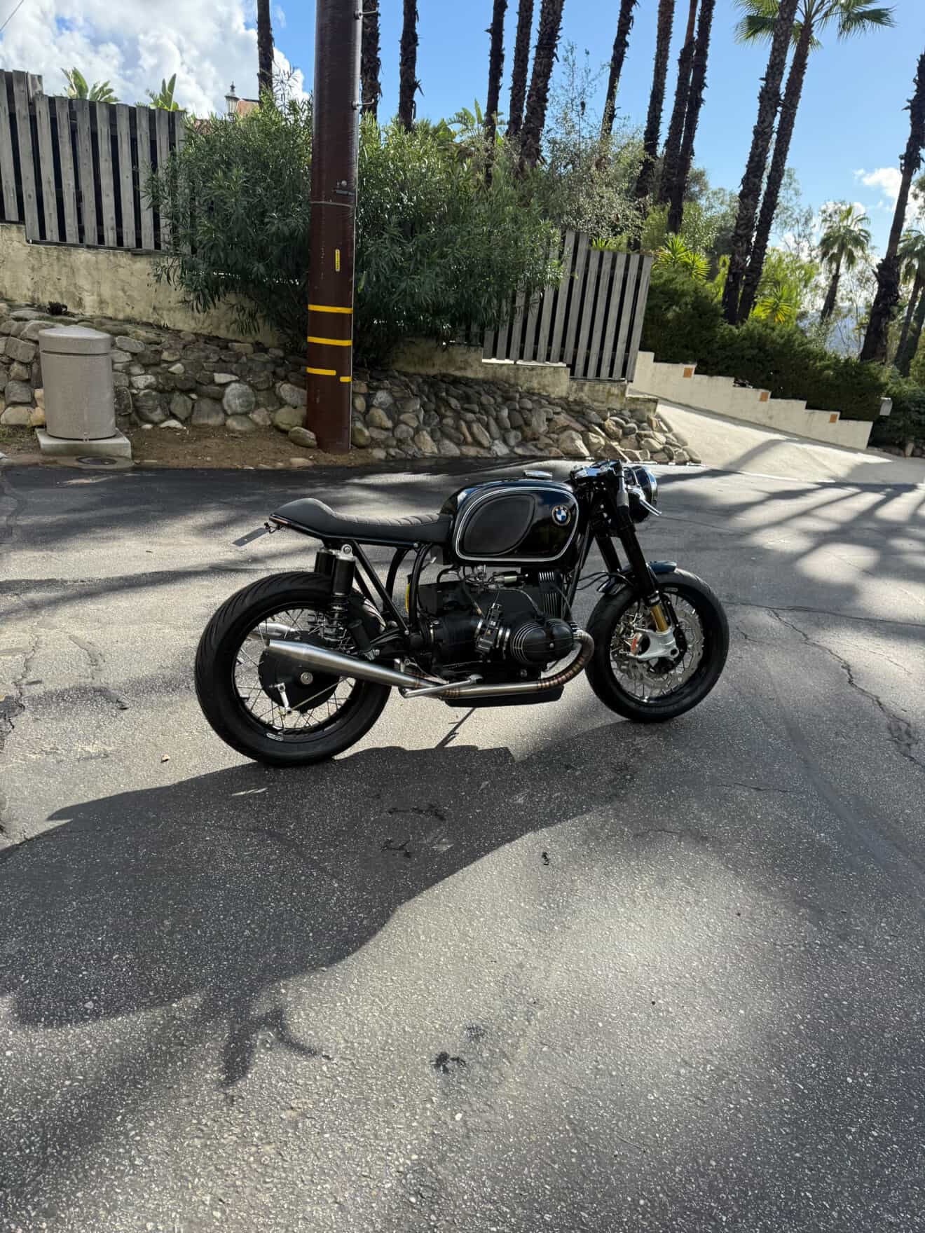 Left-side view of the BMW airhead cafe racer with the MAD Exhausts system, street with wooden fence