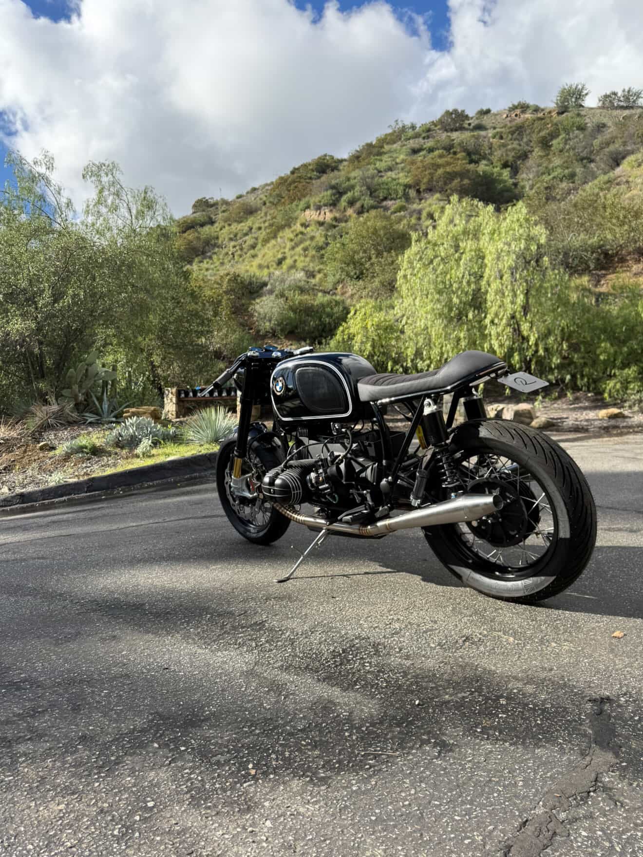 Rear-right view of the BMW airhead cafe racer with MAD Exhausts cone muffler, scenic hillside road
