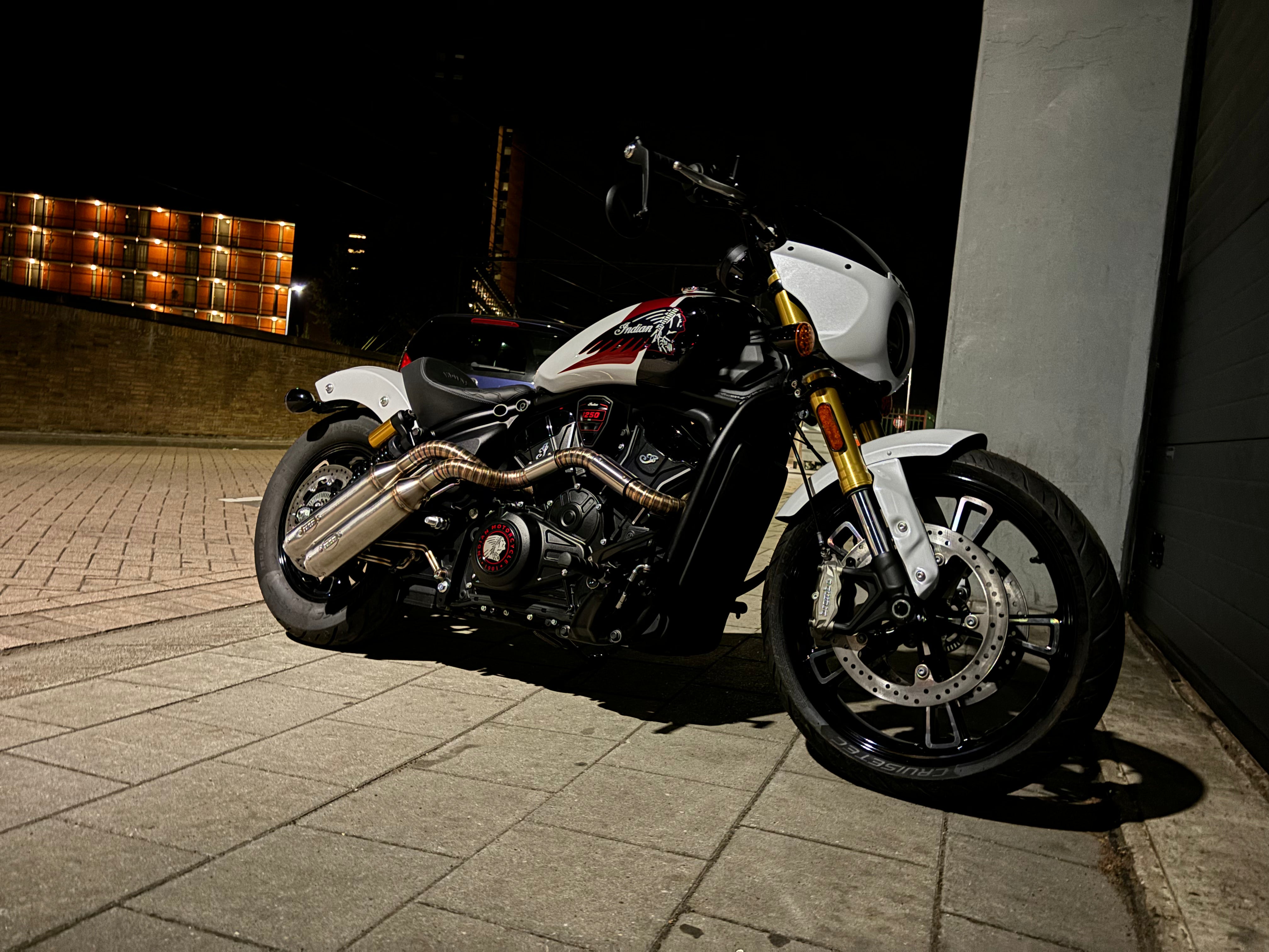 White and red Indian Scout 1250 fitted with the MAD Exhausts down-swept system, front three-quarter view at night