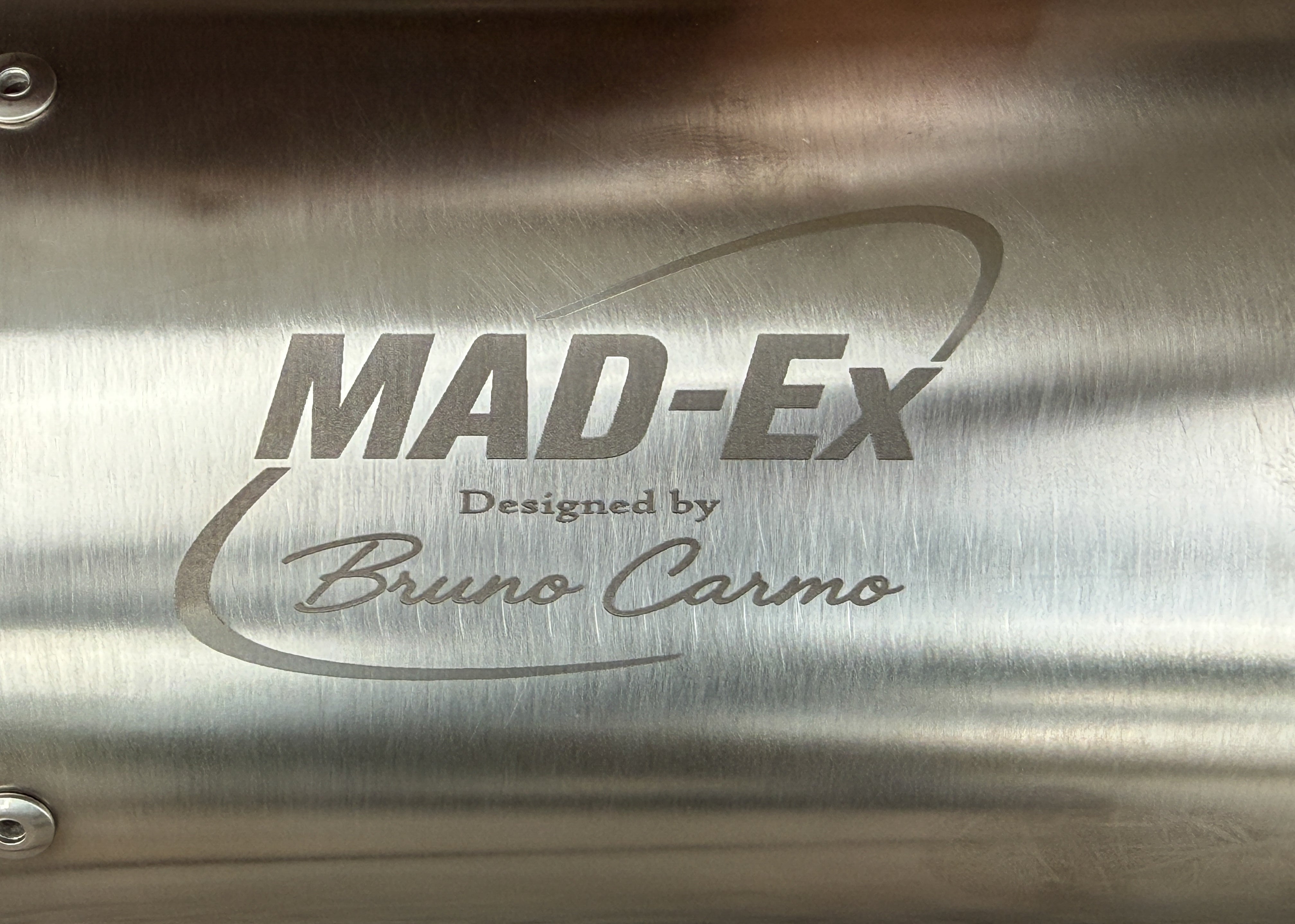 Close-up of the MAD-EX Designed by Bruno Carmo engraving on the brushed stainless steel muffler body