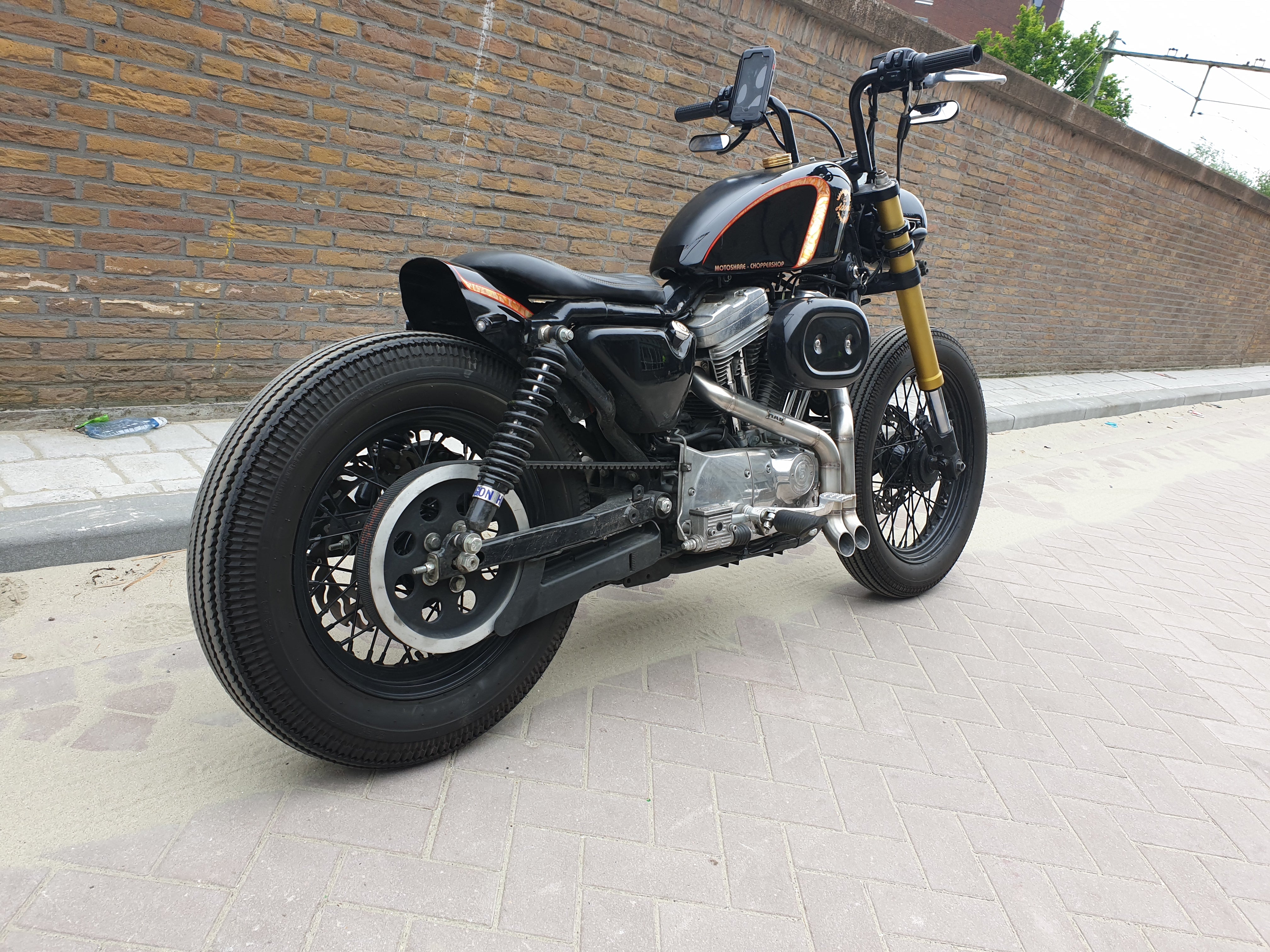 Black Harley-Davidson Sportster bobber with gold forks fitted with the MAD Exhausts system, rear three-quarter view on the street