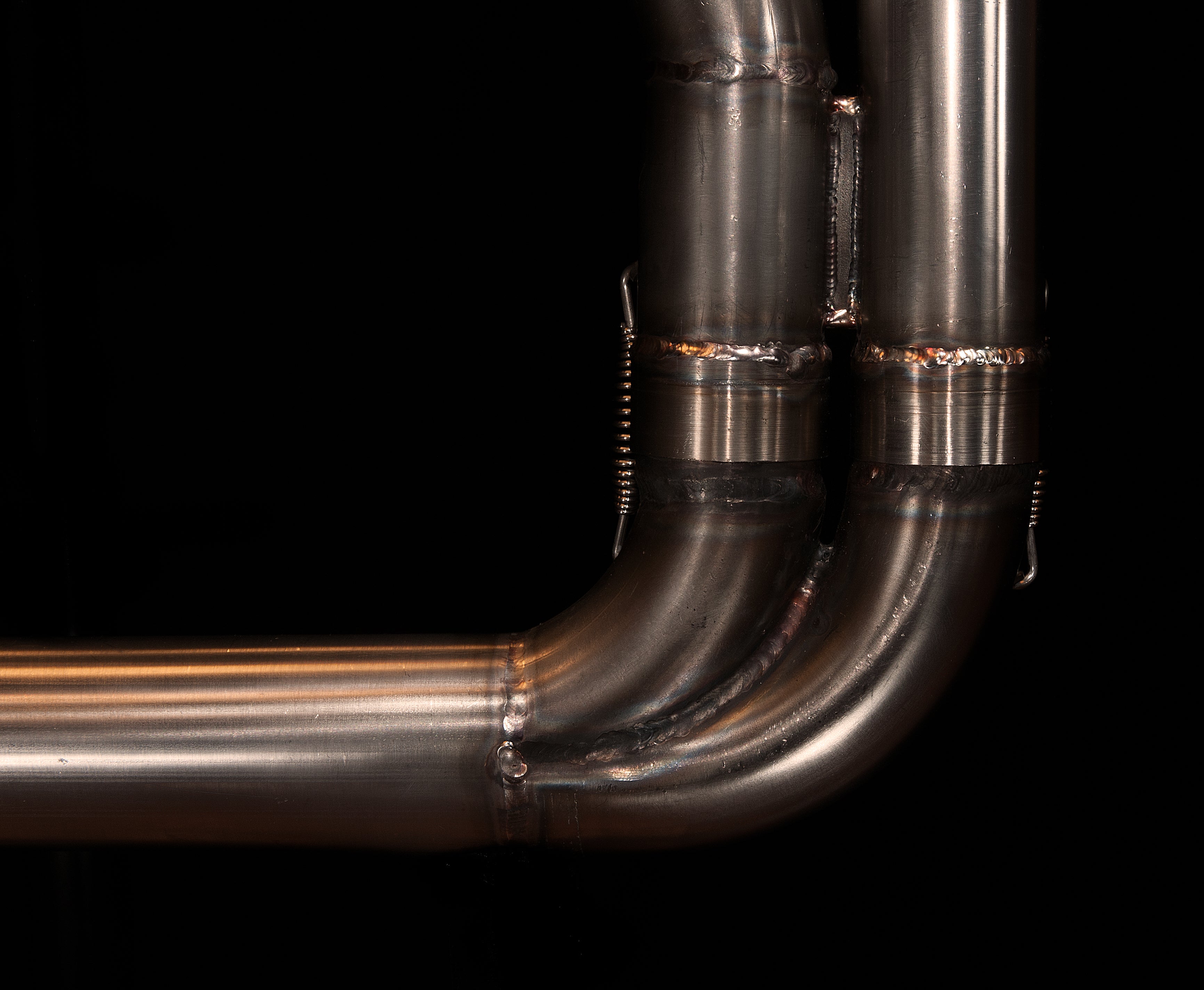 Close-up of the hand-welded 2-in-1 junction and spring mounts on the MAD Exhausts Harley-Davidson Sportster header, studio photo on black