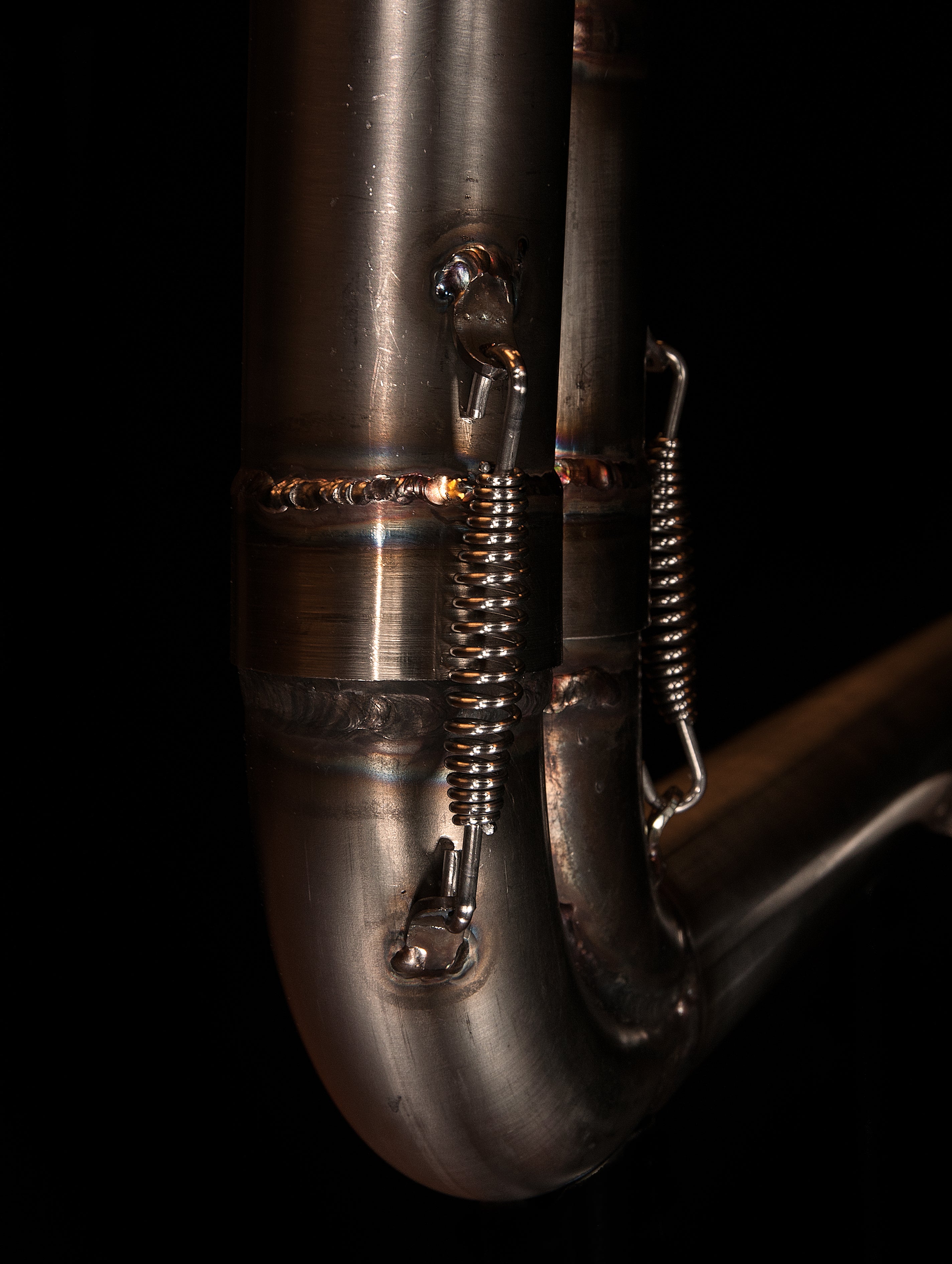 Detail of the spring mounts and welds on the MAD Exhausts Harley-Davidson Sportster collector, studio photo on black