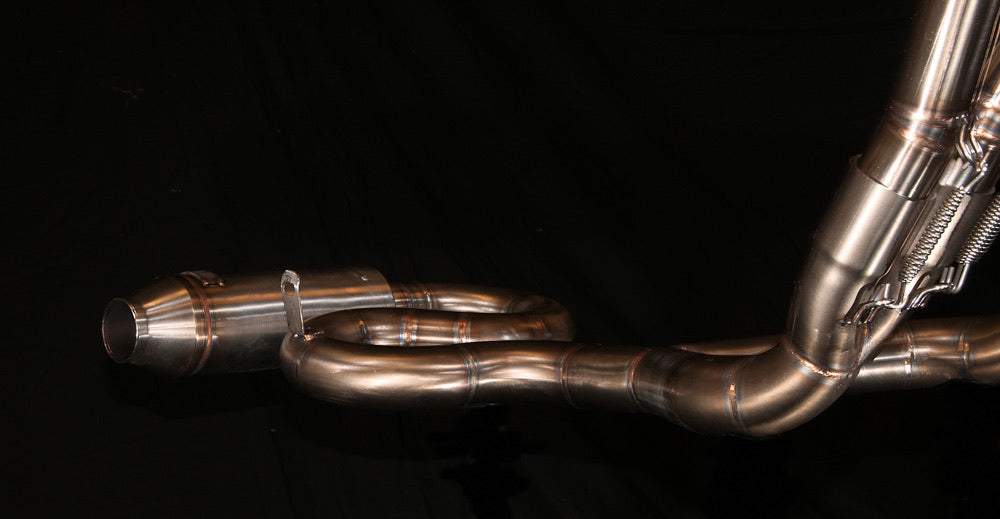 Detail of the MAD Exhausts Honda CB750 Cobra collector and muffler stub with its snake-shaped bends, studio photo on black