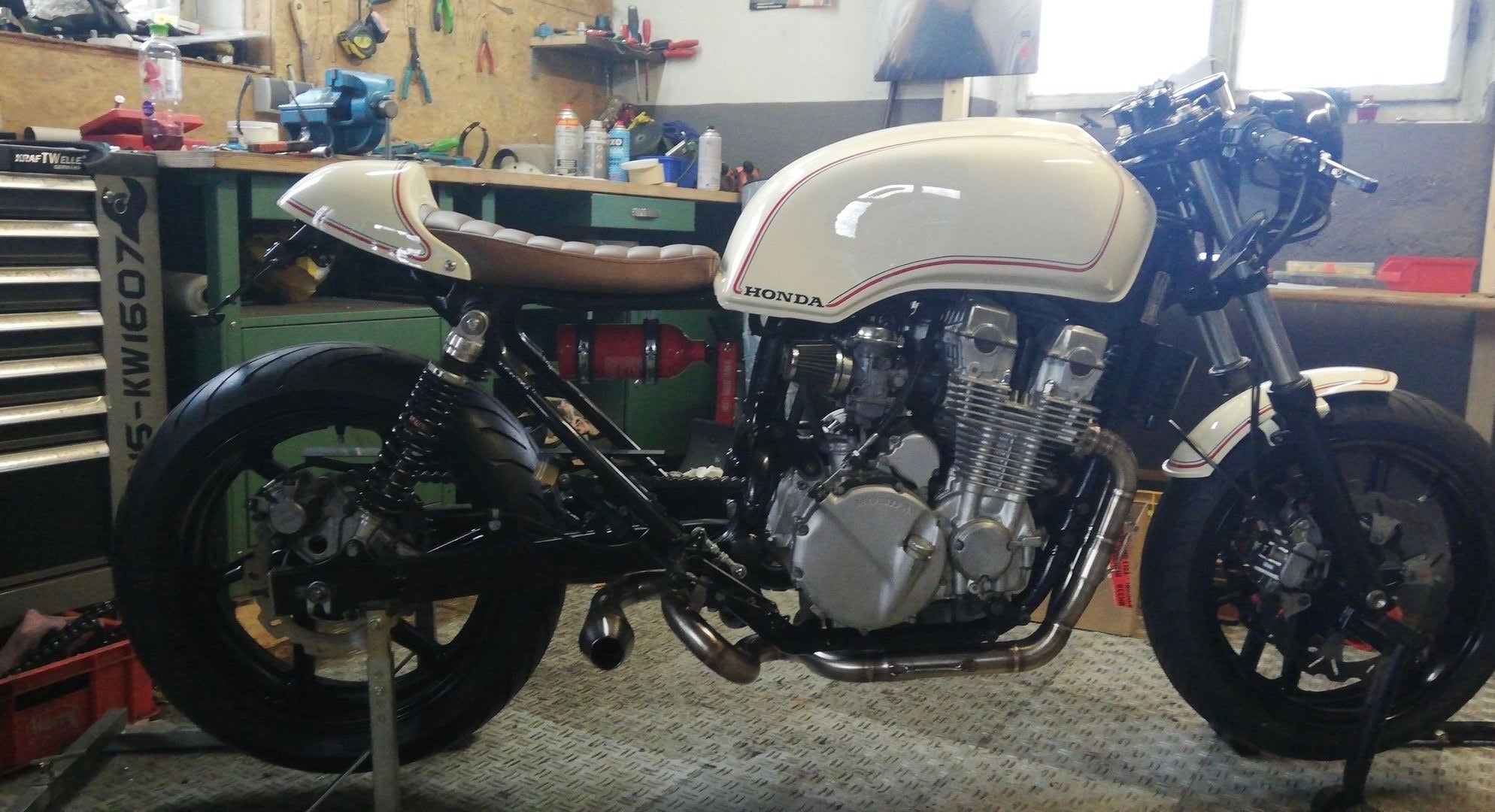 Honda CB750 cafe racer with cream and red tank fitted with the MAD Exhausts Cobra exhaust system, full side view in the workshop